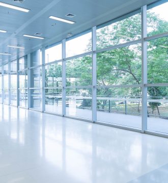 Blurred abstract background interior view looking out toward to empty office lobby and entrance doors and glass curtain wall with frame - blue white balance processing style